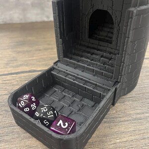 May include: A black plastic dice tower with a brick pattern. The tower is open and four dice are inside. The dice are black with white numbers and have a purple glitter finish. The dice show the numbers 10, 20, 12, and 2.
