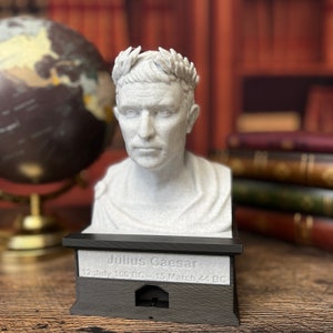 Puede incluir: Un busto de Julio César impreso en 3D con una corona de laurel. El busto está sobre una base negra con la inscripción "Julio César 12 de julio de 100 a. C. - 15 de marzo de 44 a. C.".
