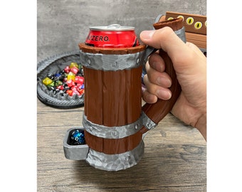Puede incluir: Una jarra de cerveza marrón y plateada con asa, que sostiene una lata roja de Zero. La jarra tiene una bandeja para dados incorporada y está diseñada para parecer un barril de madera. Una bandeja de dados coloridos está en el fondo.