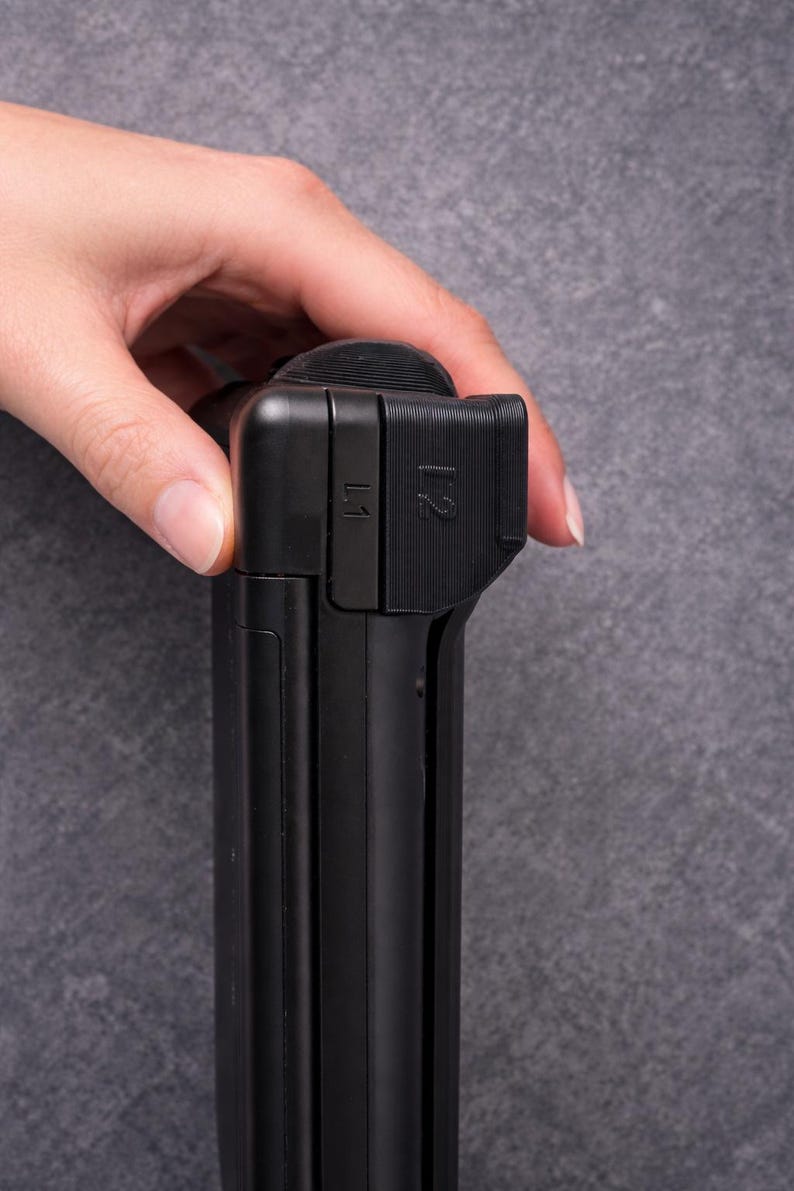 May include: A black gaming controller component featuring L1 and L2 shoulder buttons. The device has a matte finish with textured grip areas on the top section. The L1 and L2 labels are clearly embossed on the side of the black plastic housing.