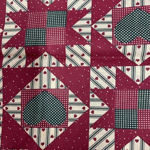 Puede incluir: Primer plano de una tela de patchwork con un patrón repetitivo. El diseño presenta cuadrados burdeos con lunares blancos, corazones y detalles a rayas. El centro de cada cuadrado tiene un patrón de corazón o cuadrado.