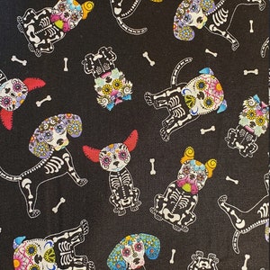 Pode incluir: Tecido preto com um padrão repetido de cães de caveira de açúcar coloridos. Os cães são esqueléticos e têm flores e outras decorações em suas caveiras. O fundo é preto com acentos brancos em forma de osso.