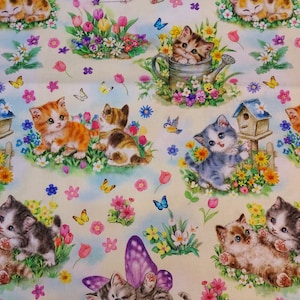 Op de afbeelding: Een witte stof met een herhalend patroon van kittens in verschillende poses. De kittens worden omringd door kleurrijke bloemen, vlinders en een vogel. Sommige kittens dragen feeënvleugels. De stof is perfect voor knutselprojecten zoals quilts, kussens en draagtassen.