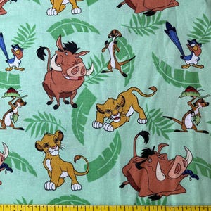 Könnte beinhalten: Ein grüner Stoff mit einem sich wiederholenden Muster aus Zeichentrickfiguren aus dem Film Der König der Löwen. Die Figuren sind Simba, Pumbaa, Timon und Zazu. Der Stoff ist perfekt für Bastelprojekte wie Quilts, Kissen und Tragetaschen.