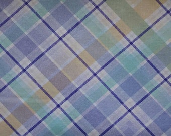 May include: A close-up of a fabric with a plaid pattern. The design features intersecting lines in shades of blue, purple, green, and yellow, creating a grid-like arrangement. The fabric has a soft, slightly textured appearance.