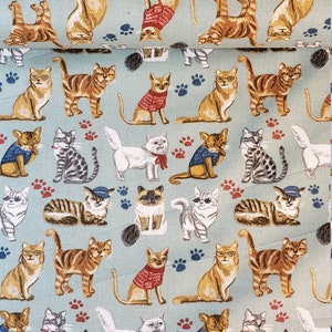May include: Fabric with a repeating pattern of various cats in different poses and outfits, including sweaters and hats. The cats are in shades of brown, gray, and white, set against a light blue background with paw prints.