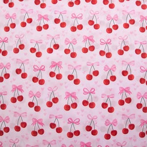 Peut inclure: Motif répété de cerises rouges avec des nœuds roses sur fond rose clair. De petits cœurs blancs sont dispersés en arrière-plan. Les cerises sont par paires et par trois.