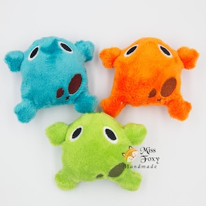 May include: Three plush toys in shades of blue, orange, and green. Each toy has a rounded shape with four appendages and brown spots. The toys have black oval eyes and are made of soft, fuzzy material. The toys are handmade.
