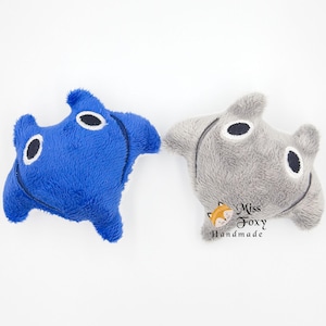 May include: Two plush toys shaped like manta rays. One is a vibrant blue, the other is gray. Both have black and white eye details and a stitched mouth. The toys are on a white background.