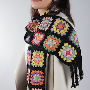 May include: A black crochet scarf with colorful granny squares. The scarf has fringe on the ends.
