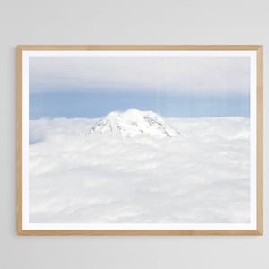 May include: A snowy mountain peak rises above a sea of white clouds. The sky is a pale blue, with a hint of sunlight.