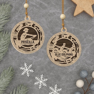 Peut inclure: Deux décorations de Noël en bois sur le thème nautique. L'une porte l'inscription "Priscilla" et l'autre "Blue Dolphins". Les deux ont un design circulaire avec une personne ramant dans un bateau. Elles sont suspendues à une ficelle.