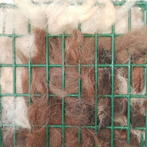 Pode incluir: Um alimentador de p&aacute;ssaros de arame verde cheio de pelo de animal marrom e branco.