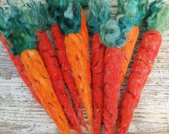 May include: A group of seven hand-felted carrots with green tops. The carrots are orange and red, and the tops are a mix of green and blue.