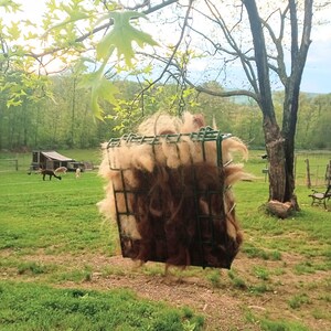 Pode incluir: Uma l&atilde; de alpaca marrom e branca pendurada em uma gaiola de arame. A gaiola est&aacute; suspensa em um galho de &aacute;rvore. A l&atilde; de alpaca &eacute; fofa e macia.