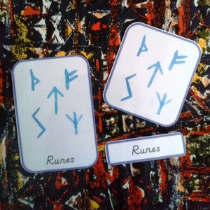 Puede incluir: Dos tarjetas blancas con bordes azules y runas azules en ellas. Las tarjetas tienen la palabra "Runes" impresa en ellas.