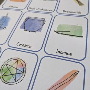 Può includere: Un set di carte stampabili con illustrazioni di vari strumenti di stregoneria, tra cui un athame, un libro delle ombre, una scopa, un calderone, incenso, un pentagramma e una bacchetta. Le carte sono bianche con bordi blu e sfondi ad acquerello.