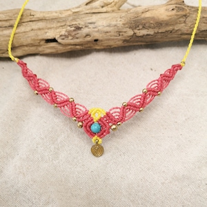 Op de afbeelding: Een roze en gele macramé ketting met een turquoise kraal en een gouden bedel.
