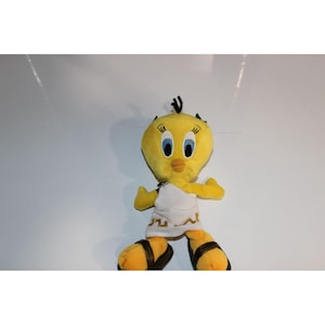 Puede incluir: Un peluche amarillo de Tweety Bird con una toga blanca y sandalias marrones. El juguete tiene ojos azules grandes, un pico naranja y pelo negro. El juguete es un personaje de dibujos animados de la serie Looney Tunes.