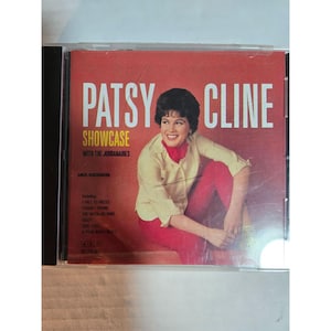 Op de afbeelding: Een cd-albumhoes van Patsy Cline's "Showcase". De hoes is rood met witte tekst. Het toont een foto van Patsy Cline in een crèmekleurige blouse en rode broek. Het album bevat nummers als "I Fall to Pieces" en "Crazy".