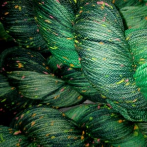 May include: Close-up of several skeins of green yarn with flecks of yellow, orange, and pink. The yarn appears to be a thick, textured wool, perfect for knitting or crocheting projects. The color variation gives the yarn a unique, speckled appearance.