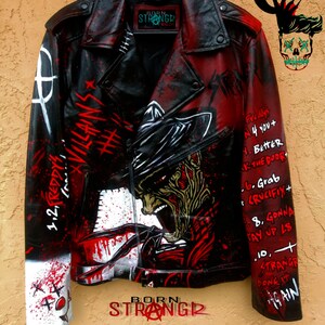 Könnte beinhalten: Eine schwarze Lederjacke mit roten und weißen Farbstichen. Die Jacke zeigt ein Motiv von Freddy Krueger aus der Filmreihe Nightmare on Elm Street. Der Text "Born Stranger" ist auf der Jacke geschrieben.