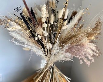 May include: A dried flower bouquet with a mix of beige, brown, and white dried grasses and flowers. The bouquet is tied together at the base with a natural twine.