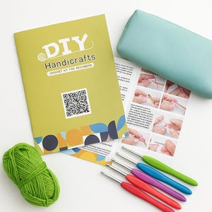 Pode incluir: Um kit de croch&ecirc; artesanal DIY para iniciantes. O kit inclui uma bola de l&atilde; verde, agulhas de croch&ecirc; com cabos coloridos, um estojo azul claro e um livreto com instru&ccedil;&otilde;es.