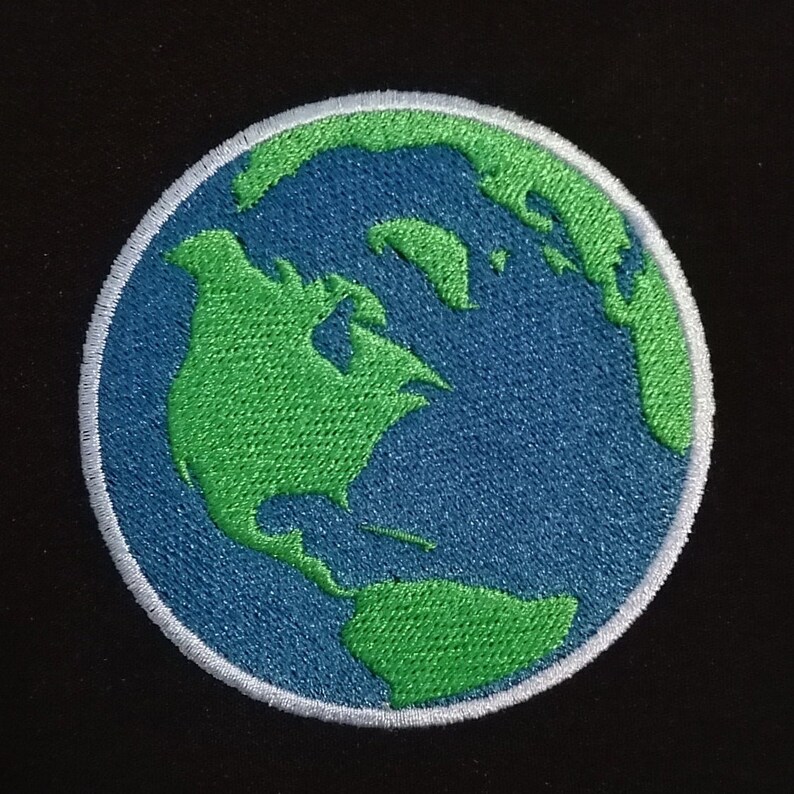May include: Embroidered patch showing a detailed depiction of Earth. The design features the continents in green against a blue ocean, with a white border. Suitable for clothing or accessories.