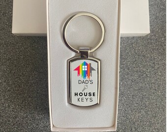 May include: A silver keychain with a rectangular tag featuring a rainbow house design and the text "Dad's House Keys".