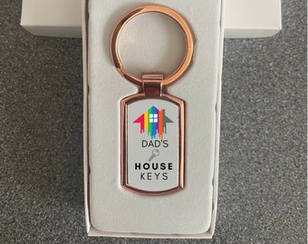 May include: Rose gold key chain with a rectangular tag that says "Dad's House Keys" with a rainbow house graphic and a key icon.