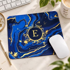 May include: A rectangular mouse pad featuring a deep blue and navy marble pattern with gold veining accents. In the centre, a gold circular frame with ornate flourishes surrounds the capital letter E printed in a bold, gold serif font.
