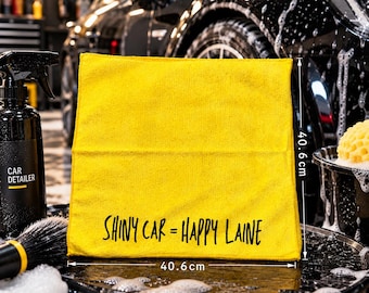May include: A square yellow microfiber cleaning cloth featuring the black text "SHINY CAR = HAPPY LAINE" printed on the front. The cloth measures 16 inches by 16 inches, as indicated by the white dimension lines and labels visible on the image.