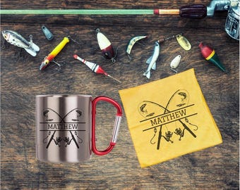 May include: A stainless steel mug with a red handle and the name "Matthew" printed on it, along with a yellow cloth with a fishing-themed design. Various fishing lures and a fishing rod are arranged on a wooden surface.