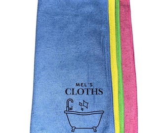 May include: A set of four microfiber cleaning cloths in blue, green, yellow, and pink. The cloths are folded and stacked, with the blue cloth on top. The blue cloth has the text "MEL'S CLOTHS" and a bathtub icon printed on it.