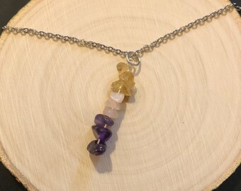 May include: A silver chain necklace with a pendant made of stacked, natural gemstones. The stones are yellow, pink, and purple.