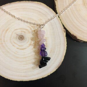 May include: A silver chain necklace with a pendant made of layered gemstones. The pendant features pink, purple, and black stones.