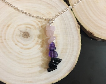 May include: A silver chain necklace with a pendant made of layered gemstones. The pendant features pink, purple, and black stones.