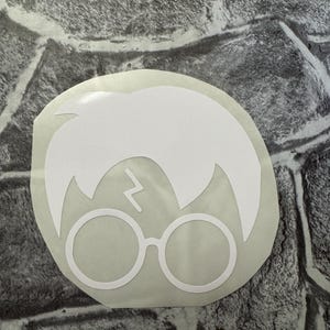 Puede incluir: Pegatina de vinilo blanco de Harry Potter con su cicatriz de rayo característica y gafas redondas.