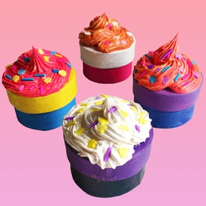 May include: Four colorful cupcake-shaped boxes with different colored frosting and sprinkles. The boxes are made of cardboard and have a purple, blue, yellow, and pink base.