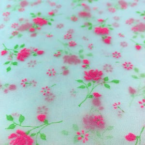 May include: A white fabric with a pink and green floral pattern. The flowers are small and delicate, and the fabric has a sheer, almost translucent quality.