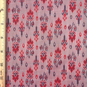 May include: Close-up of a fabric with a repeating pattern of red and dark blue floral-like shapes on a light pink background. The fabric has a textured appearance, with a grid-like weave. A wooden ruler is on the left side of the image.