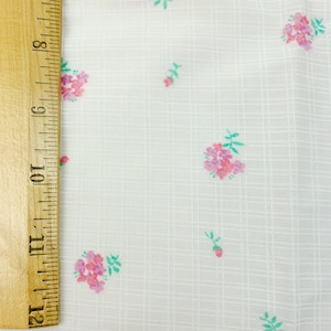 May include: White fabric with a subtle grid pattern and a scattered floral print in shades of pink and green.