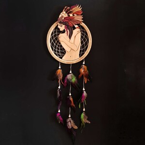 May include: A wooden dream catcher with a circular frame and a central design of a woman with feathers. The dream catcher has multiple strands of feathers hanging from the bottom.