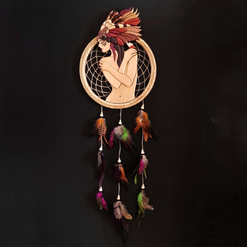 May include: A wooden dream catcher with a circular frame and a central design of a woman with feathers. The dream catcher has multiple strands of feathers hanging from the bottom.