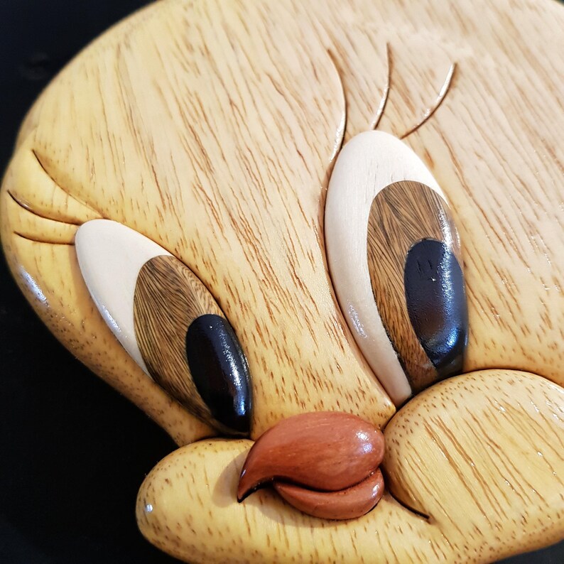Puede incluir: Primer plano de una talla de madera de Piol&iacute;n, un p&aacute;jaro de dibujos animados amarillo con ojos negros, un pico rojo y pesta&ntilde;as blancas.