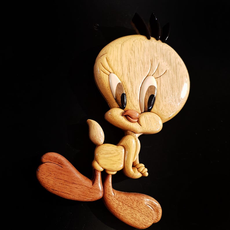 Puede incluir: Una talla de madera de Piol&iacute;n, un p&aacute;jaro de dibujos animados amarillo con ojos negros y un pico negro. La talla es detallada y realista, con una textura de veta de madera.