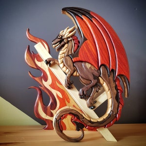 May include: A wooden dragon sculpture with red, black and brown wood grain. The dragon is perched on a wooden base with flames carved into the sides.