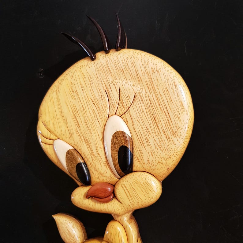 Puede incluir: Una talla de madera de Piol&iacute;n, un canario amarillo con ojos negros, un pico rojo y una pluma negra en la cabeza. La talla es detallada y realista.