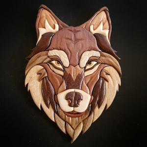 Peut inclure: Une sculpture en bois de tête de loup avec des détails complexes, réalisée à partir de différentes nuances de bois brun. Les yeux du loup sont de couleur brun clair et sa fourrure est détaillée avec des mèches de bois individuelles.